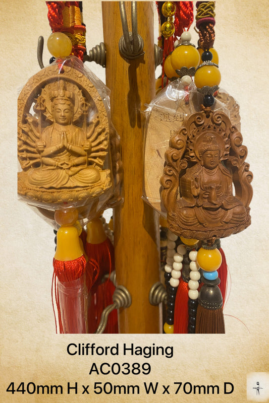 A hanging decoration featuring two brown wooden figurines of Buddhist deities, displayed against a backdrop of red and yellow beads.